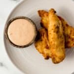 Overhead view of plate with chicken tenders on it by a small bowl of sauce.