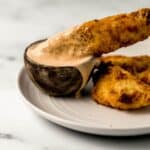 Close up side view of chicken tender being dipped in small bowl of sauce on plate.