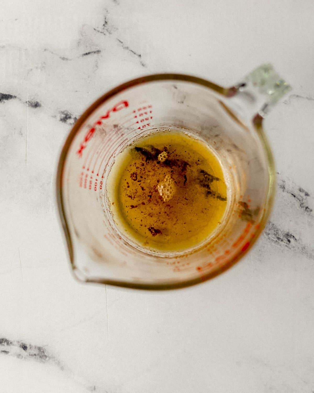 Overhead view of bacon grease in glass measuring cup on marble surface. 