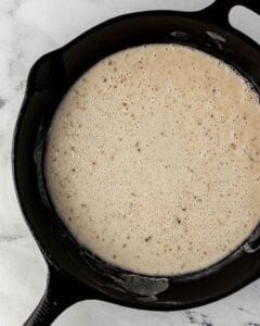 Flour added to bacon dripping in cast iron skillet.