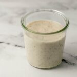 Close up side view of white gravy in a jar on marble surface.
