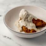 Close up side view of chicken tenders topped with gravy in white bowl.