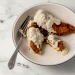 Overhead view of fried chicken tenders and gravy in white bowl with fork in it.