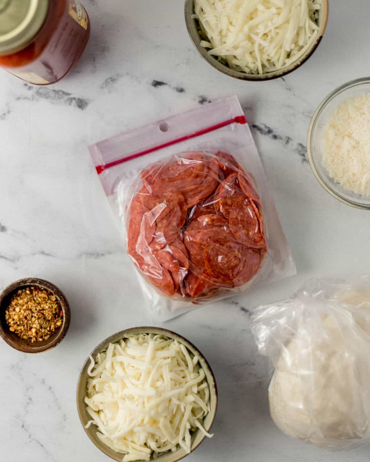 Ingredients needed to make bread in separate containers on marble surface. 