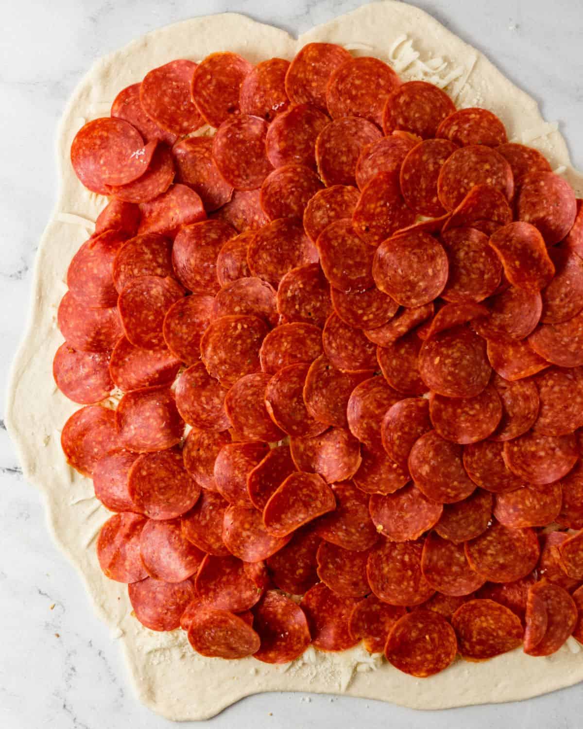 Overhead view of pepperoni added to the other ingredients on the pizza dough.