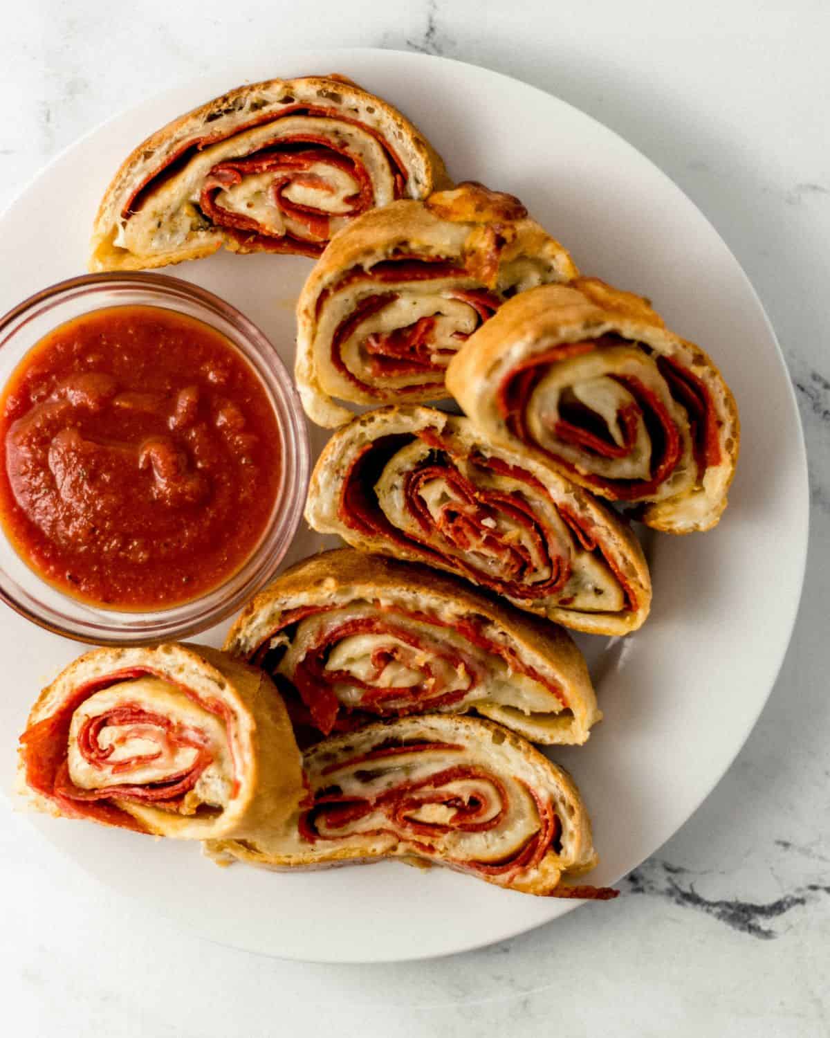 Overhead view of sliced pepperoni bread on white plate with small bowl of sauce.