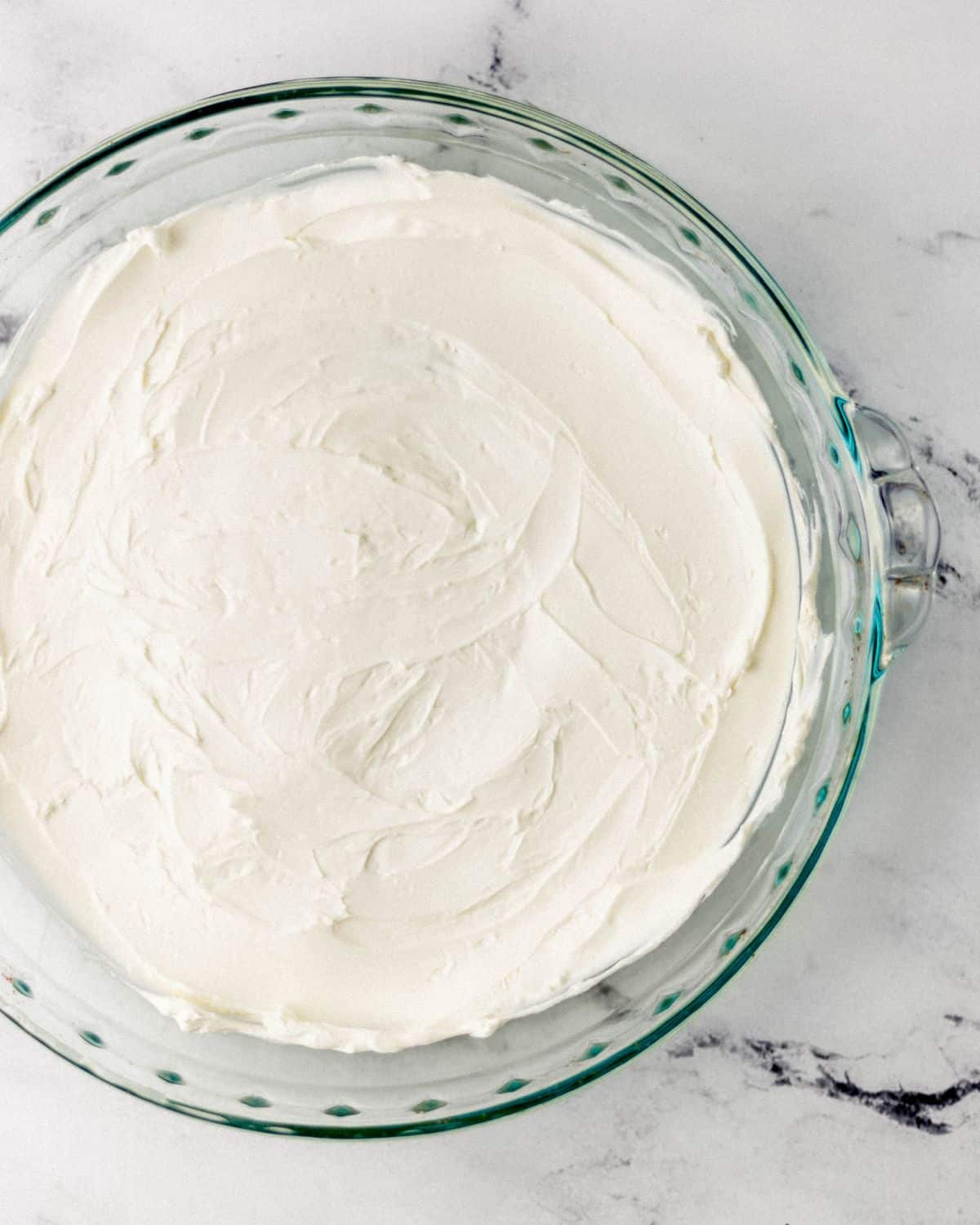 Softened cream cheese spread in the bottom of a round glass baking dish. 