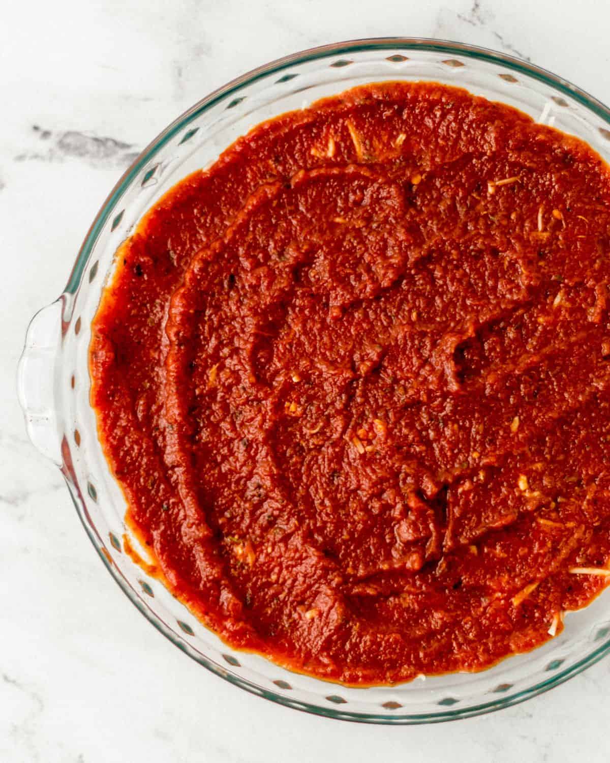 Overhead view of a layer of pizza sauce spread on top of the cheese layer of the pizza dip. 