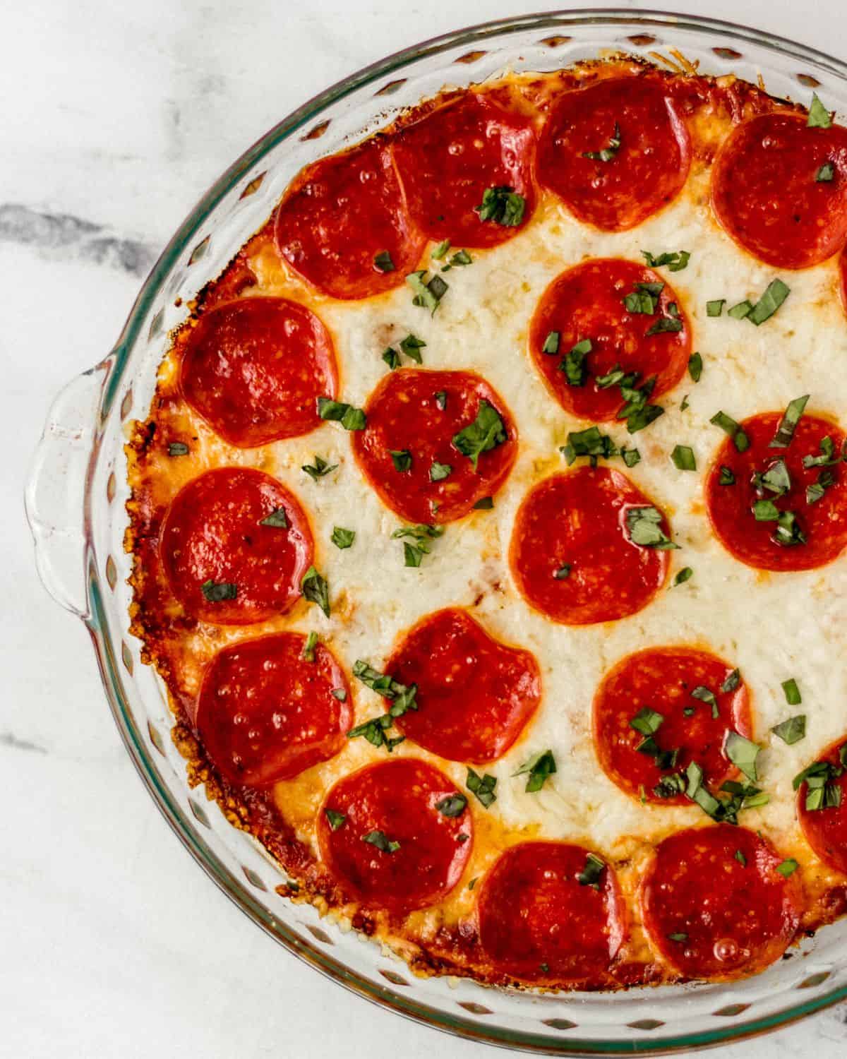 Close up overhead view of baked pizza dip topped with chopped basil in glass baking dish. 