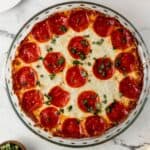 Overhead view of baked pizza dip in glass baking dish topped with chopped basil.