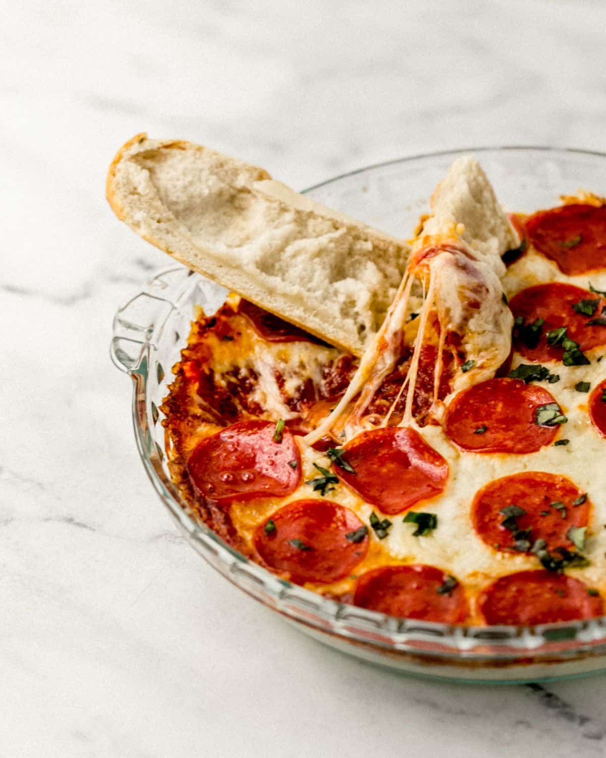 Close up front view of baked dip in glass baking dish with pieces of toasted bread in it. 