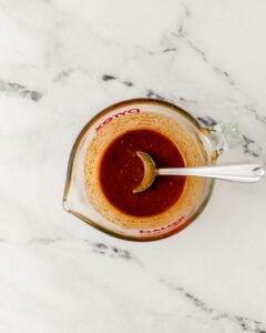 Overhead view of sauce ingredients combined in glass measuring cup with spoon.