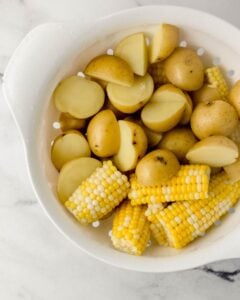 Overhead view of parboiled potatoes and corn in colander.
