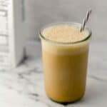 Close up side view of coffee in glass with straw in it by a carton of milk.