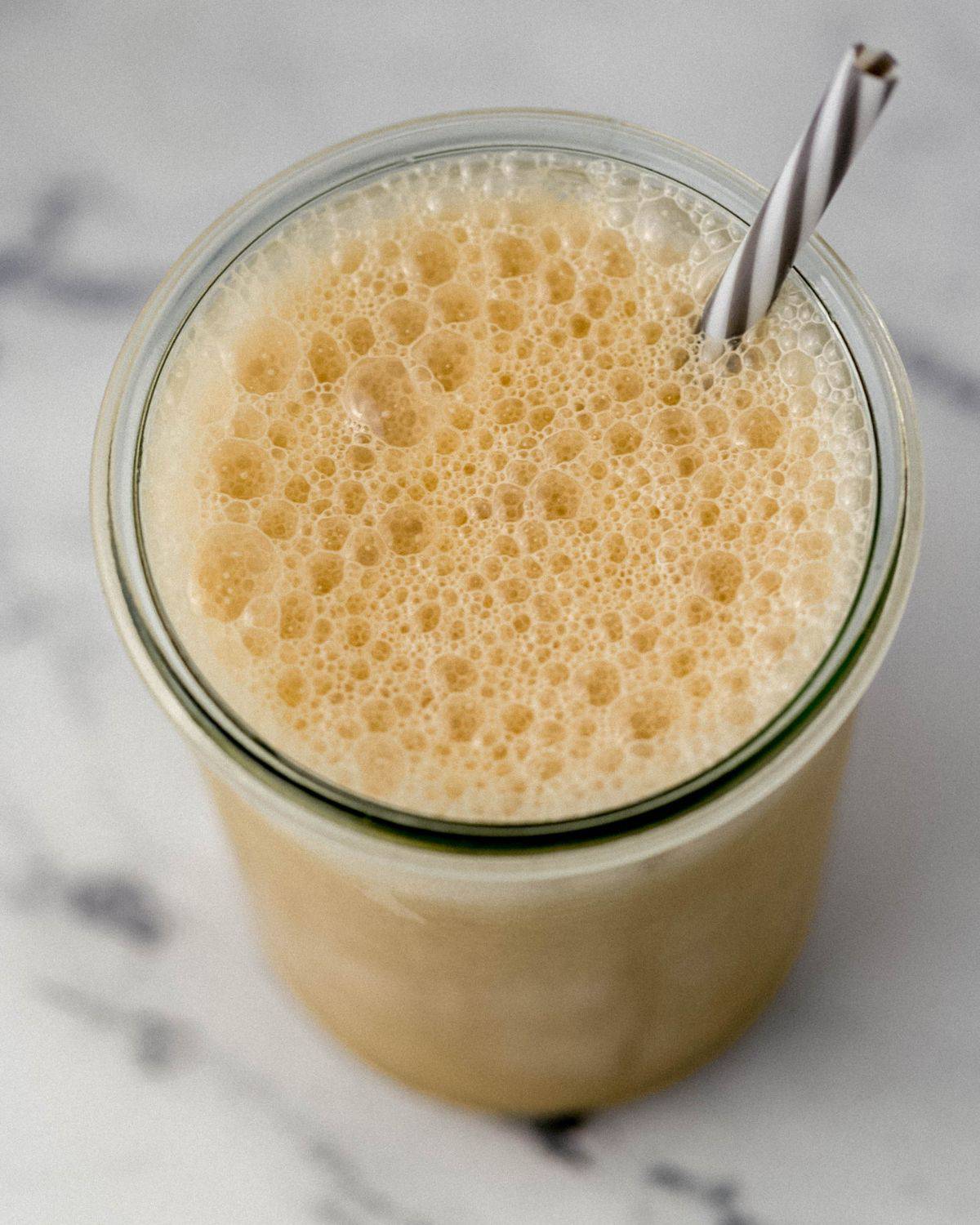 Close up view of the top of the blended drink in a glass with a straw in it. 