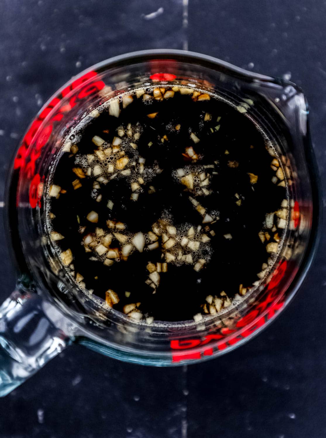 Sauce ingredients added to glass measuring cup on black tile surface. 