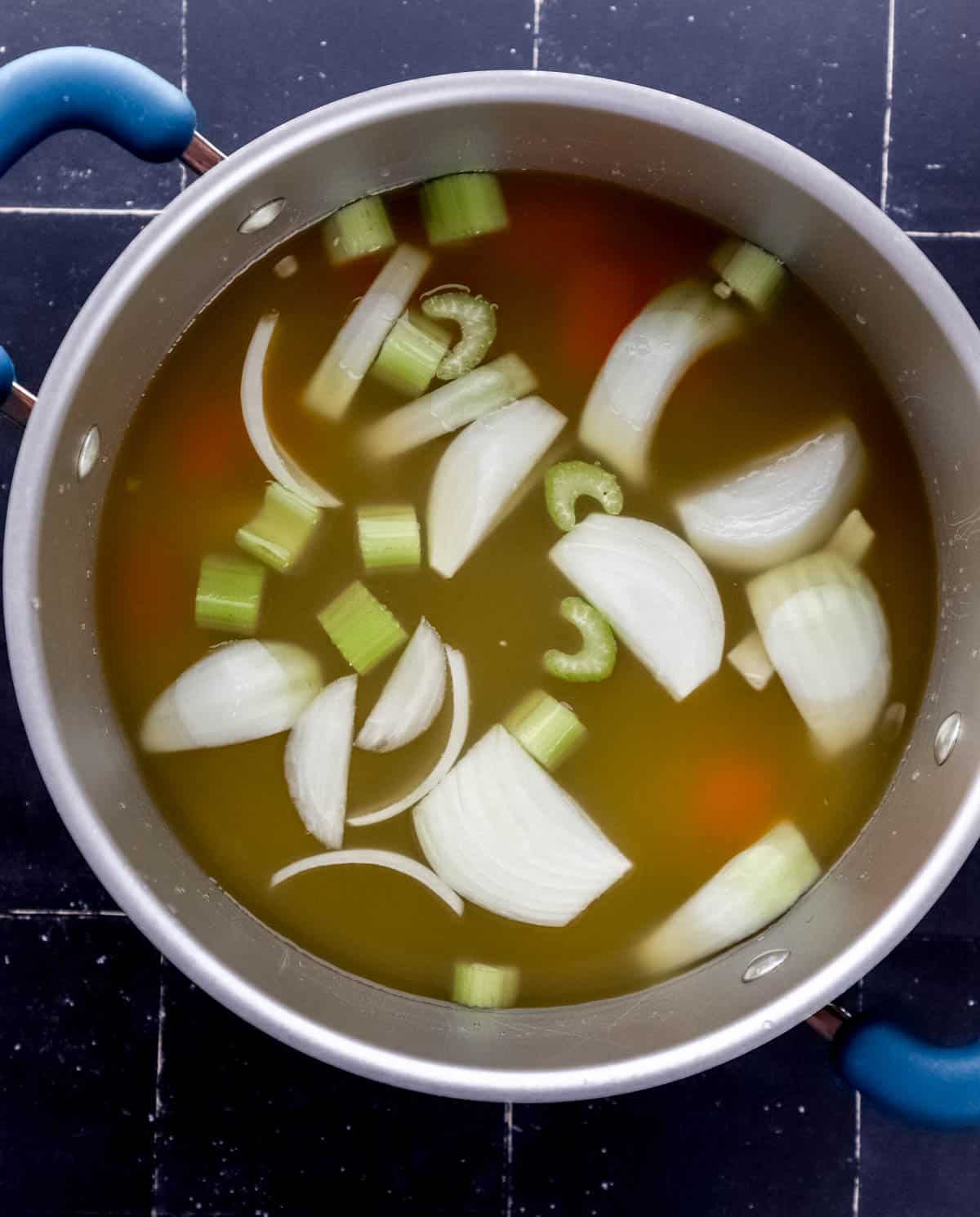 Overhead view of large pot with broth, water, and chopped vegetables in it. 