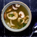 Overhead view of bowl of hibachi soup by a spoon on black tile surface.