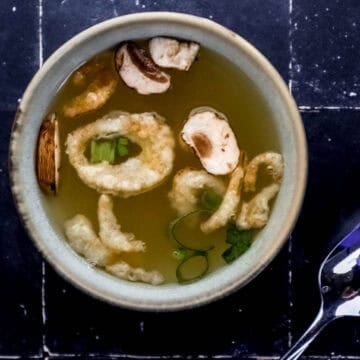 Overhead view of bowl of hibachi soup by a spoon on black tile surface.