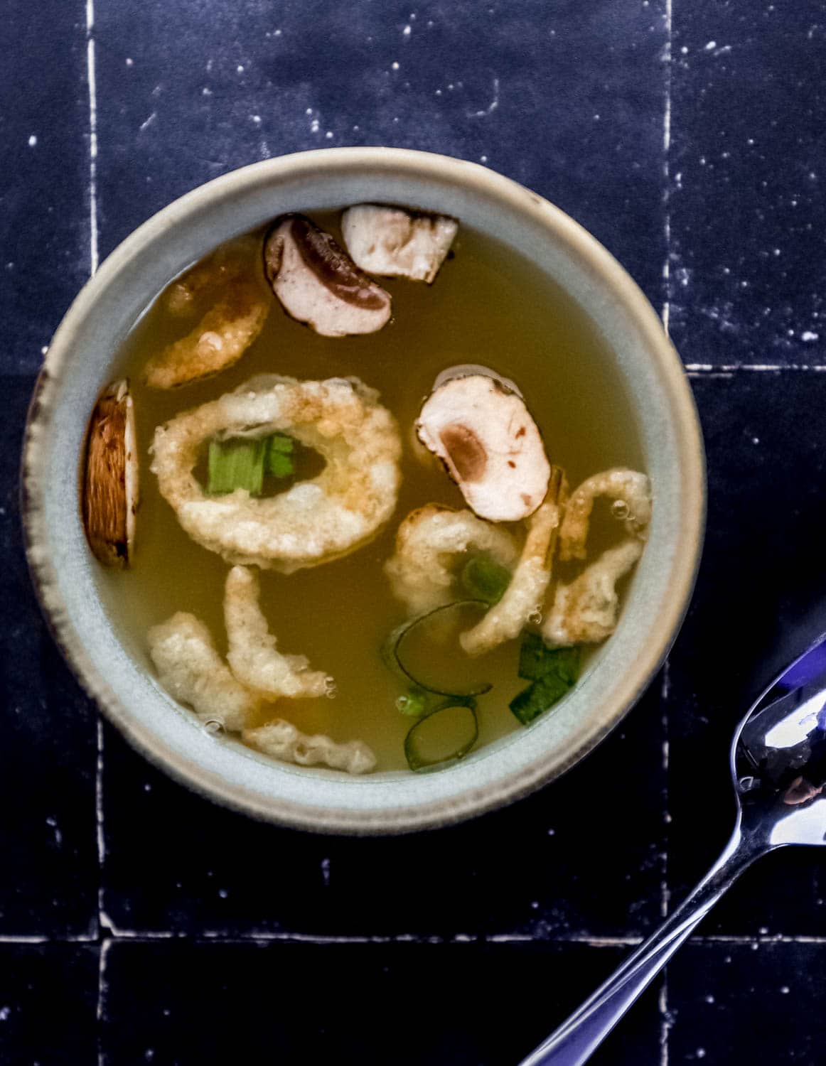 Small bowl of soup with fried onion, mushrooms, and green onion in it by a spoon. 