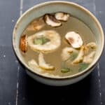 Close up front view of bowl of soup on black tile surface.