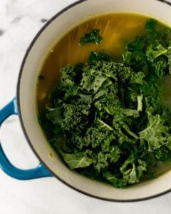 Greens and pasta added to other soup ingredients.