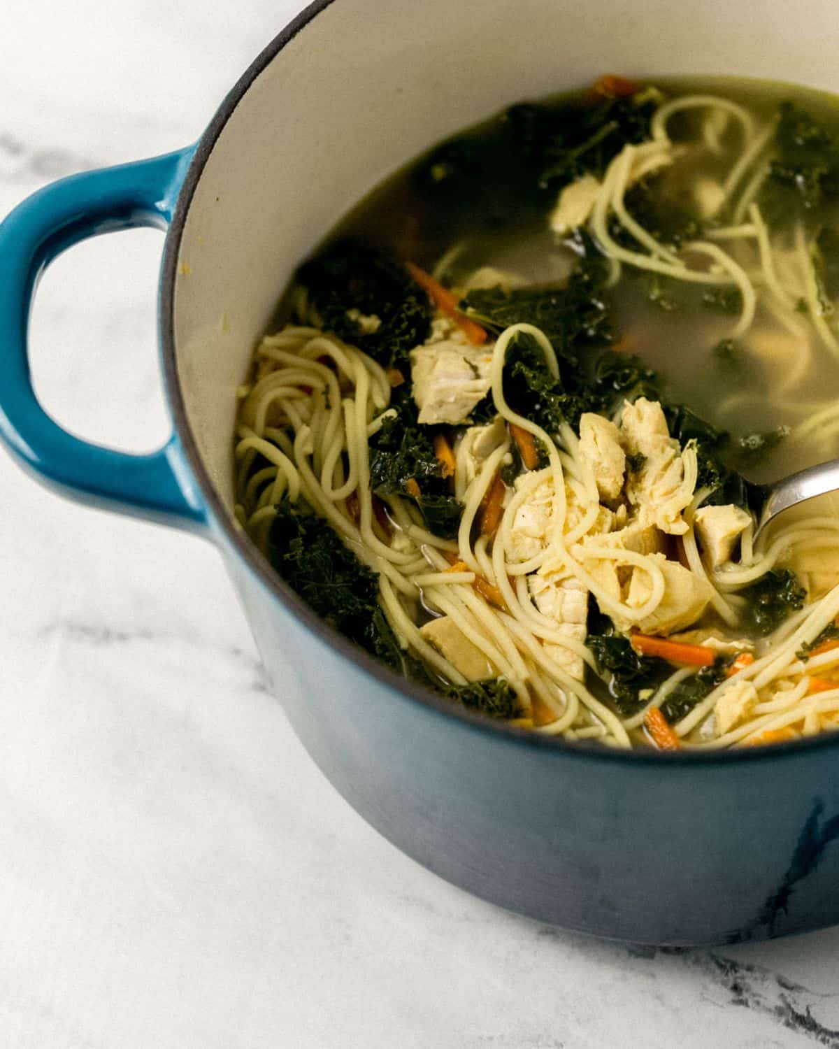 Close up front view of soup in teal dutch oven on marble surface. 