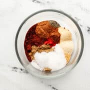 Overhead view of ingredients to make chili seasoning in glass bowl.