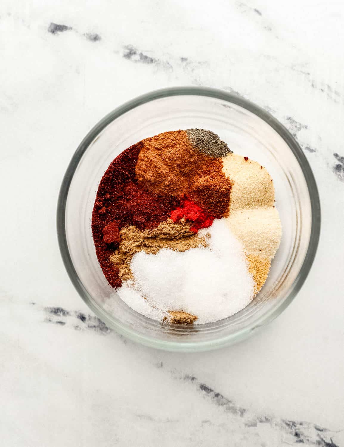 Overhead view of spiced added to small glass bowl on marble surface. 