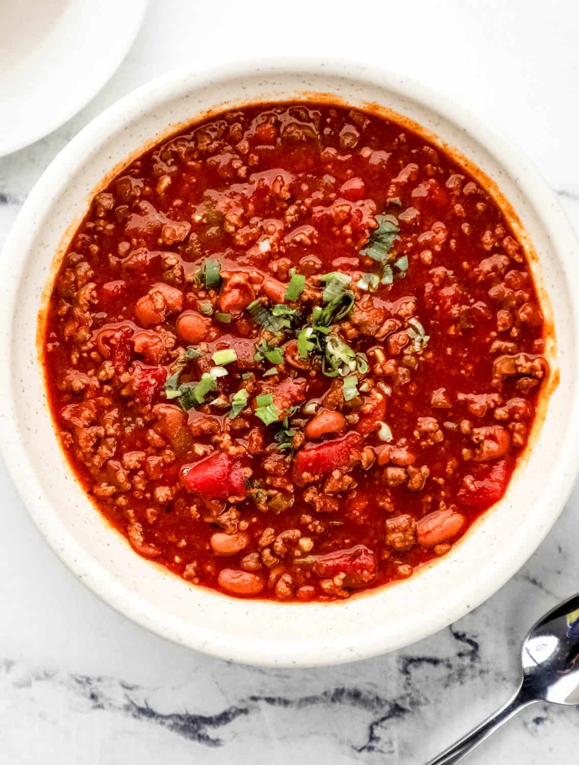 Overhead view of finished chili in a bowl topped with green onions by a spoon.