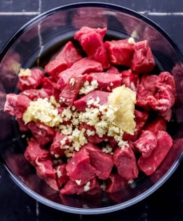 Steak and marinade ingredients added to glass mixing bowl.