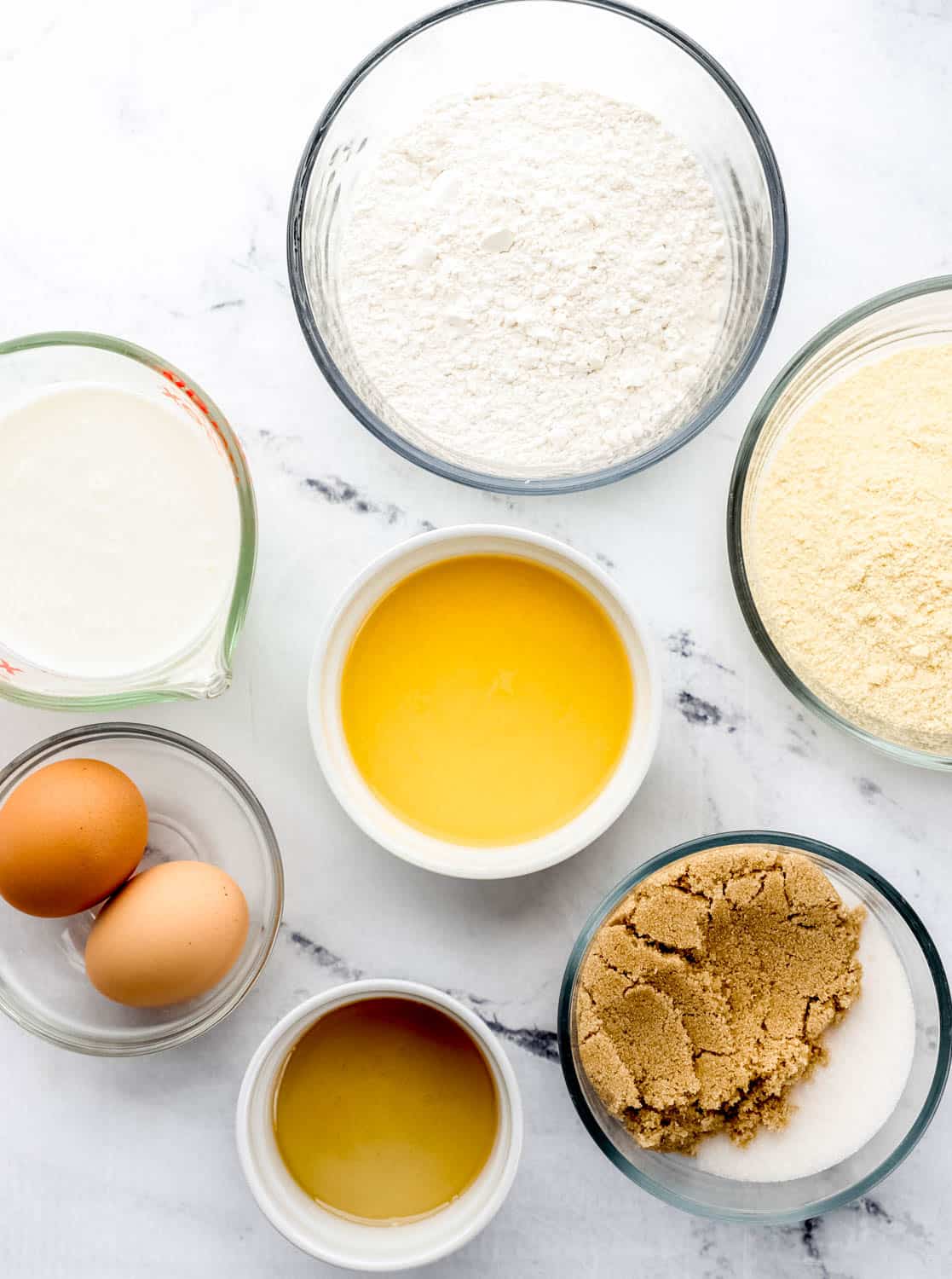 Ingredients needed to make cornbread in separate bowls on marble surface.