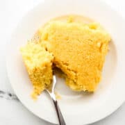 Piece of cornbread on a small white plate with a fork in it.