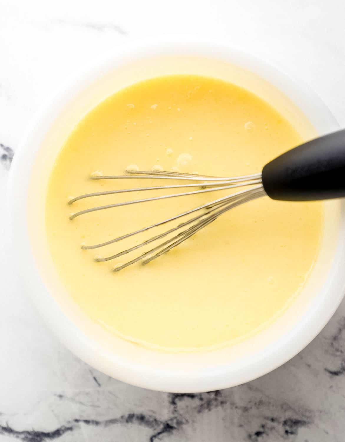 Overhead view of wet ingredients combined in white bowl with whisk.