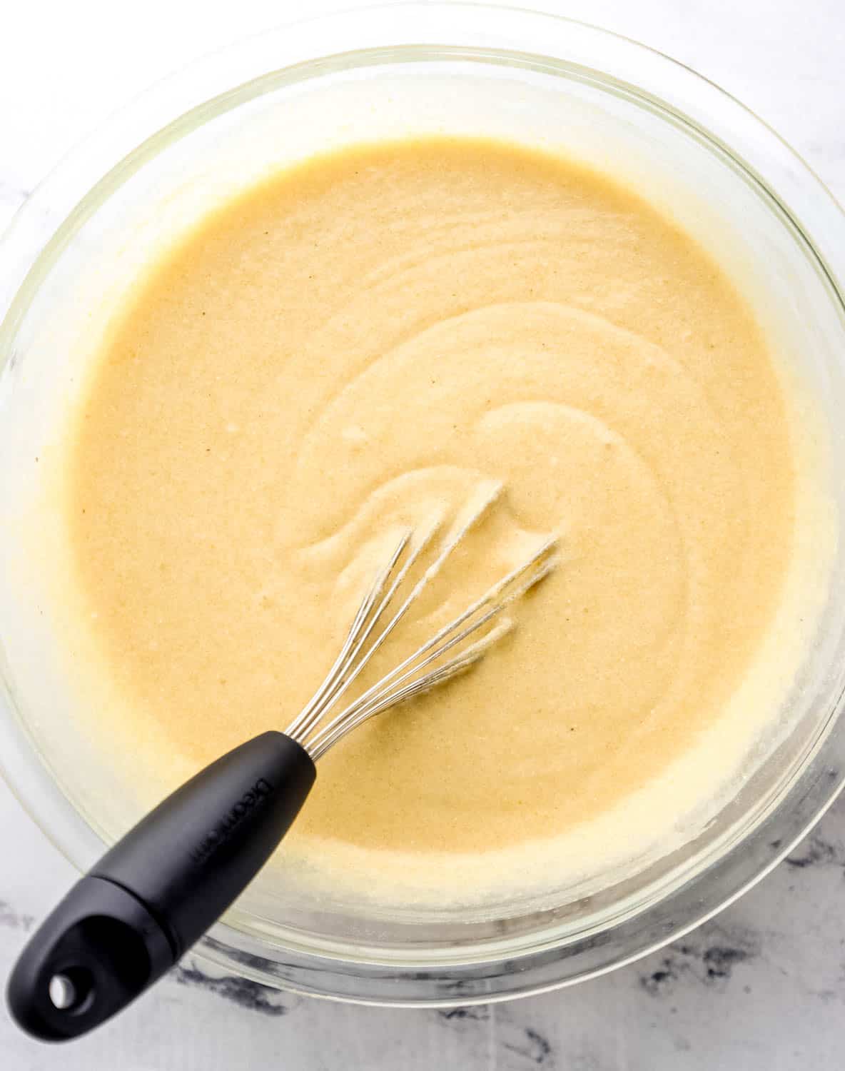 Overhead view of cornbread batter in large glass mixing bowl with whisk.