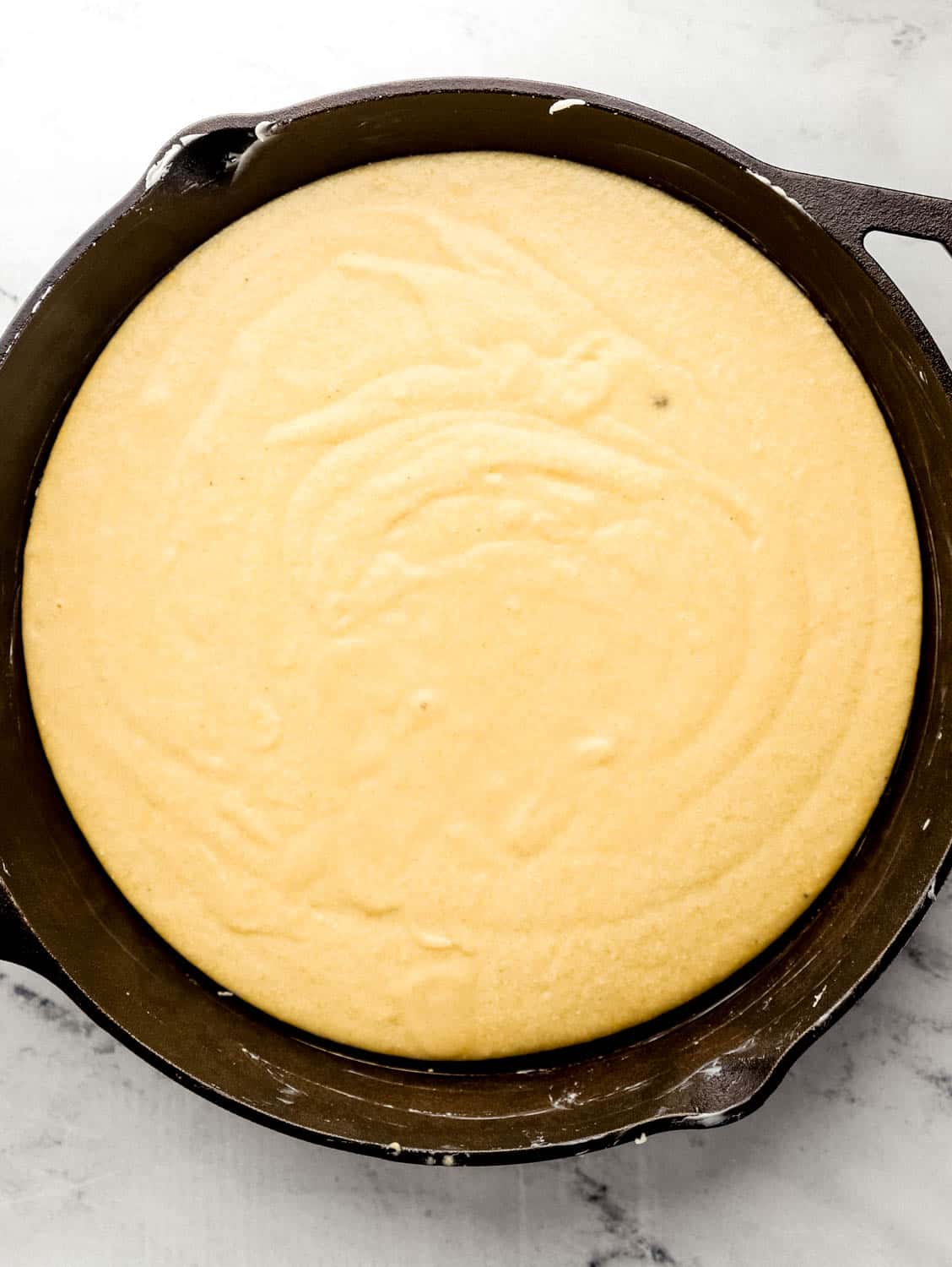 Cornbread batter poured into buttered cast iron skillet.