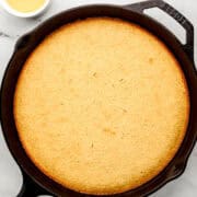 Overhead view of finished honey cornbread in cast iron skillet by small bowl of honey butter sauce.