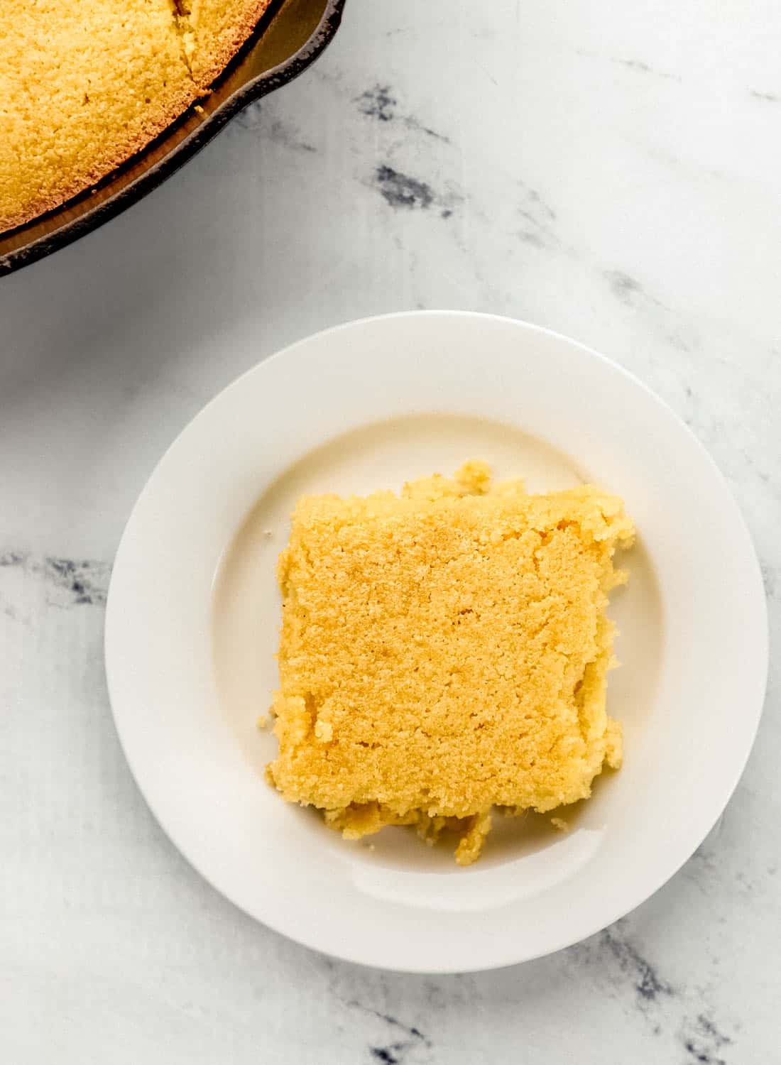 Overhead view of piece of cornbread on white plate with the rest in the background.