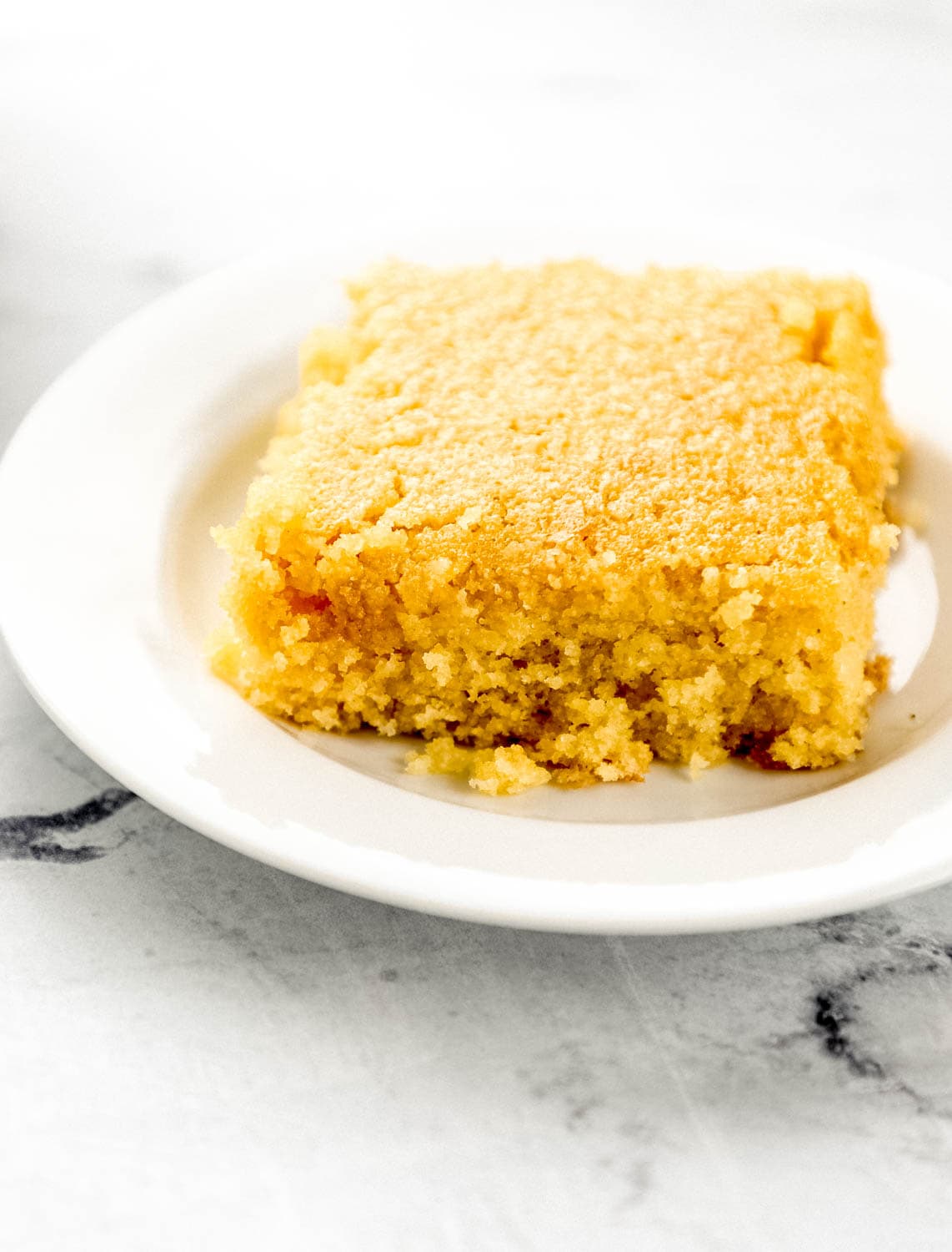 Close up front view of piece of cornbread on white plate.