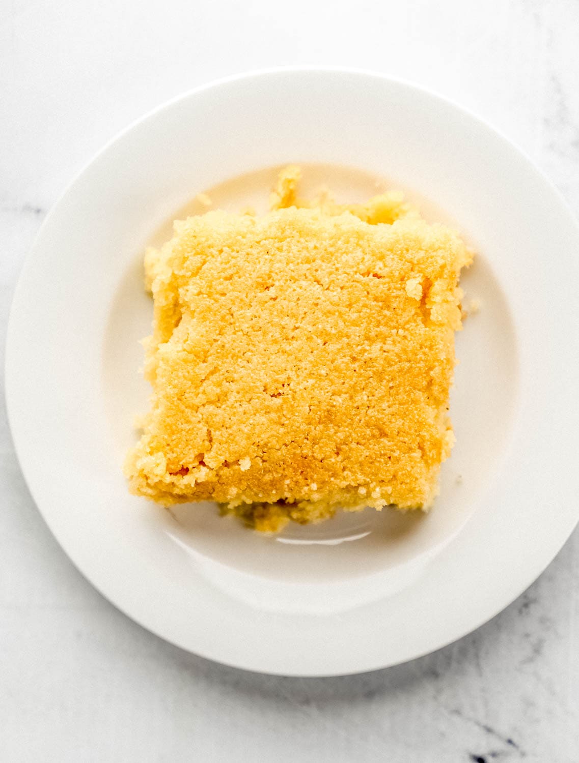 Close up overhead view of single piece of cornbread on small white plate.