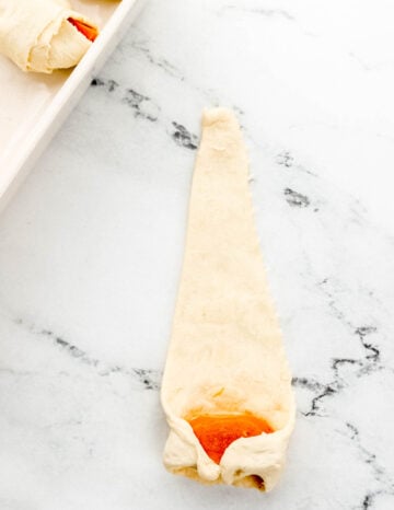 Sweet potato being rolled in piece of crescent roll dough.