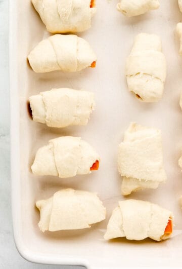 Sweet potato halves rolled in dough in baking dish.
