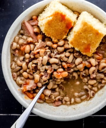 Overhead view of bowl of finished peas with spoon and cornbread in it.
