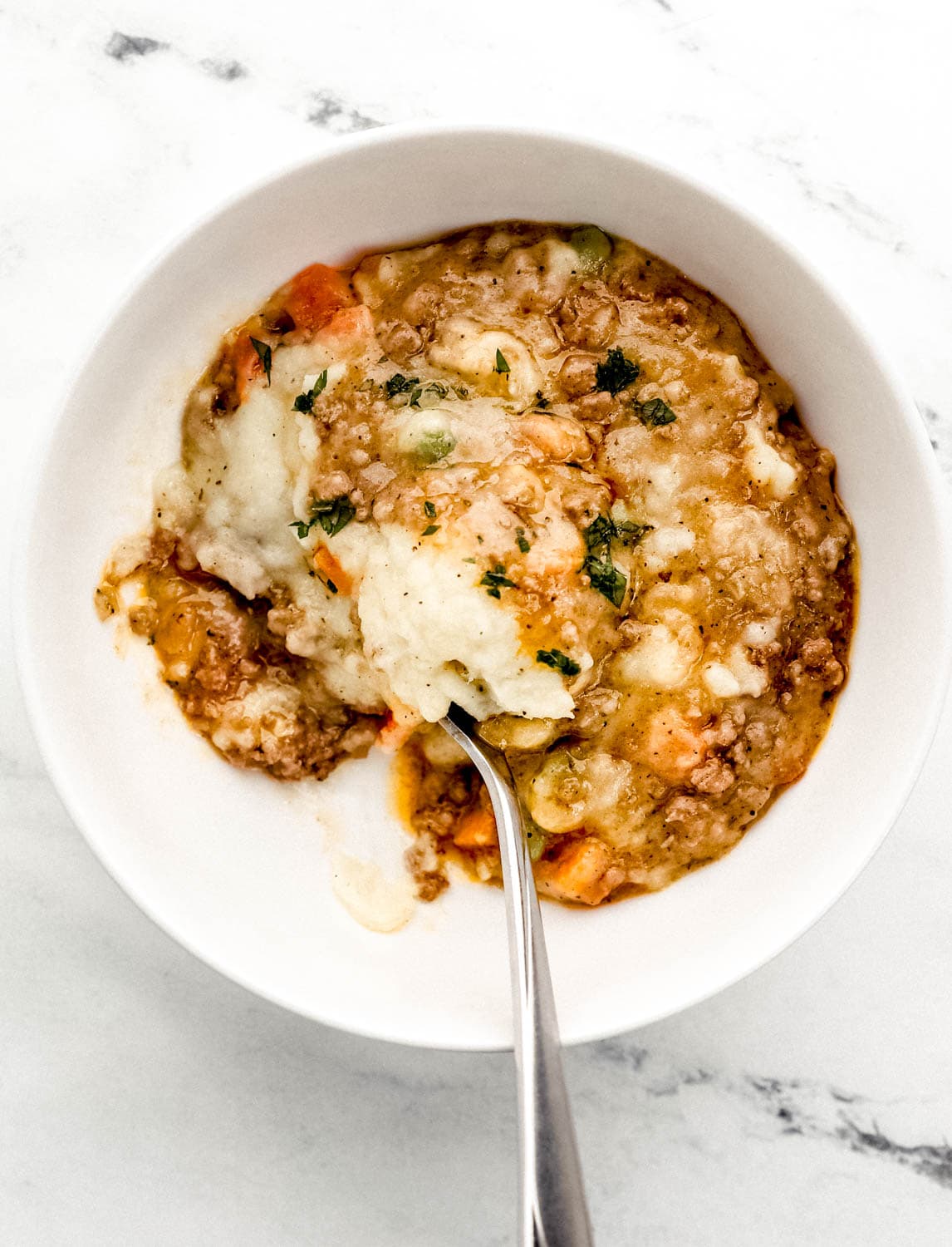White bowl with single serving of shepherd's pie and spoon in it. 