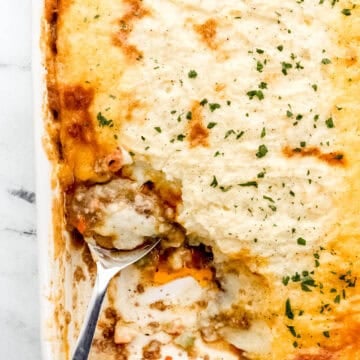 Overhead view of finished shepherd's pie in white baking dish with serving spoon in it.