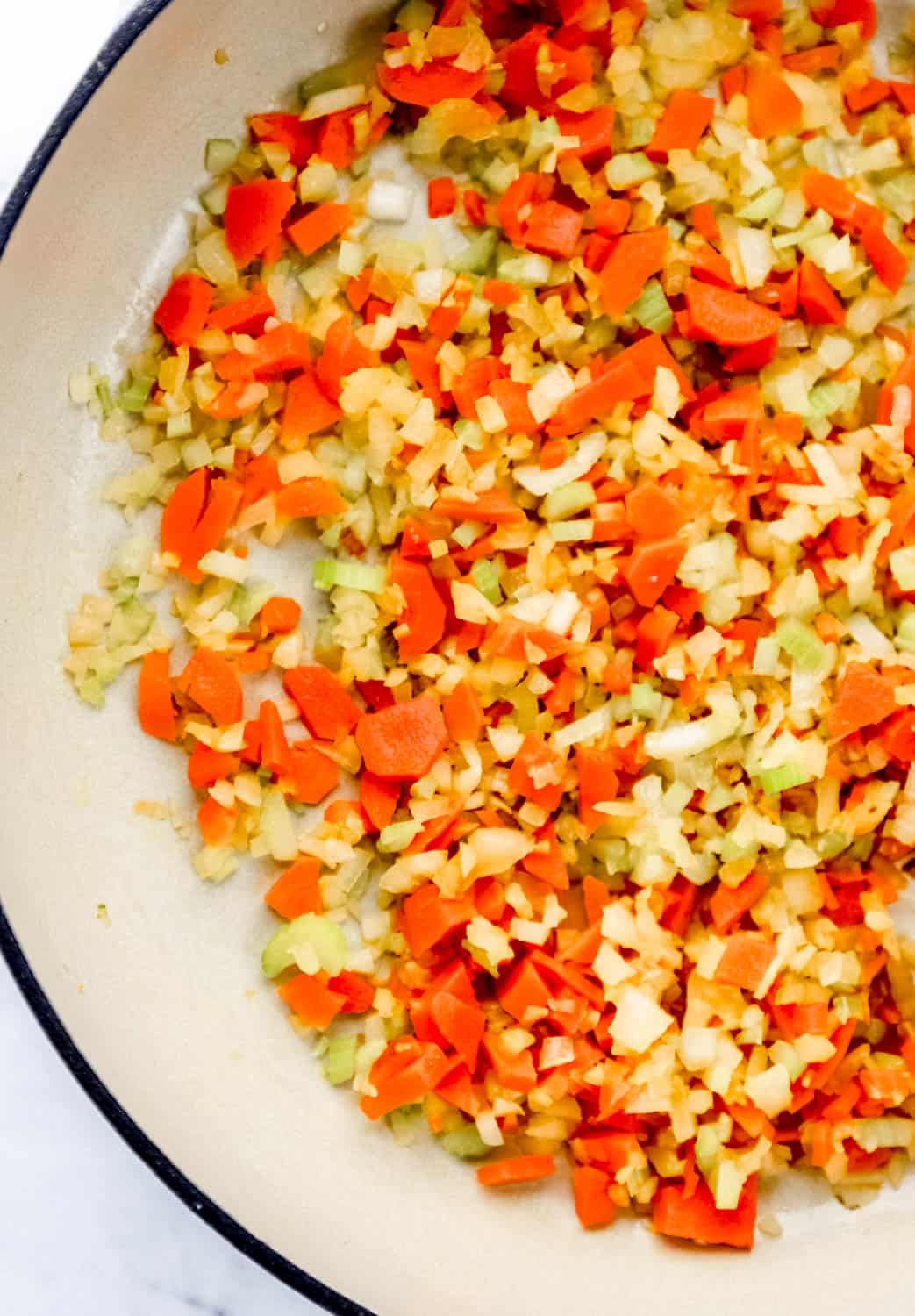 Sauteed vegetables in a large white braiser pan. 
