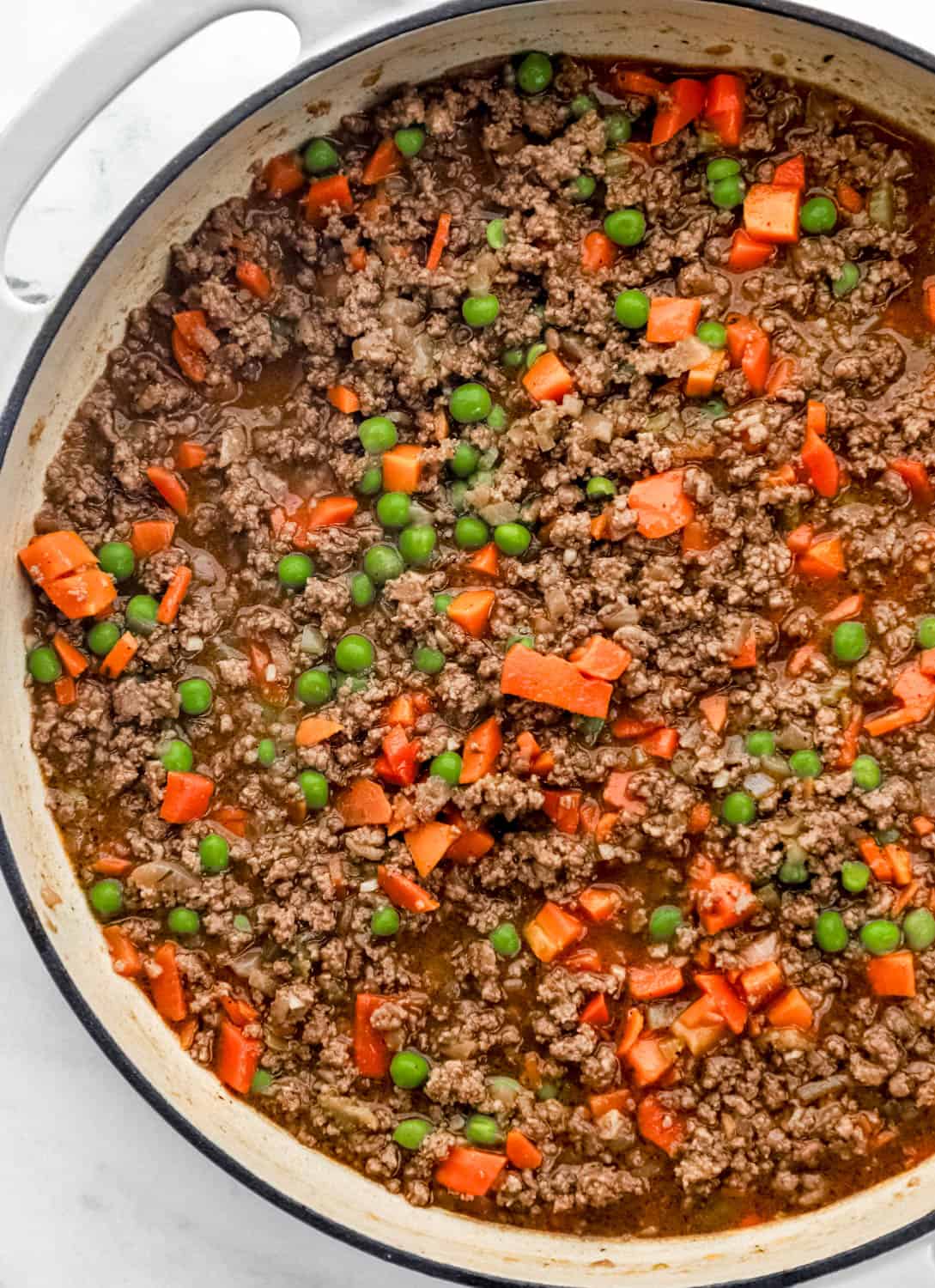 Overhead view of ground beef filling ingredients combined in large white braiser pan. 