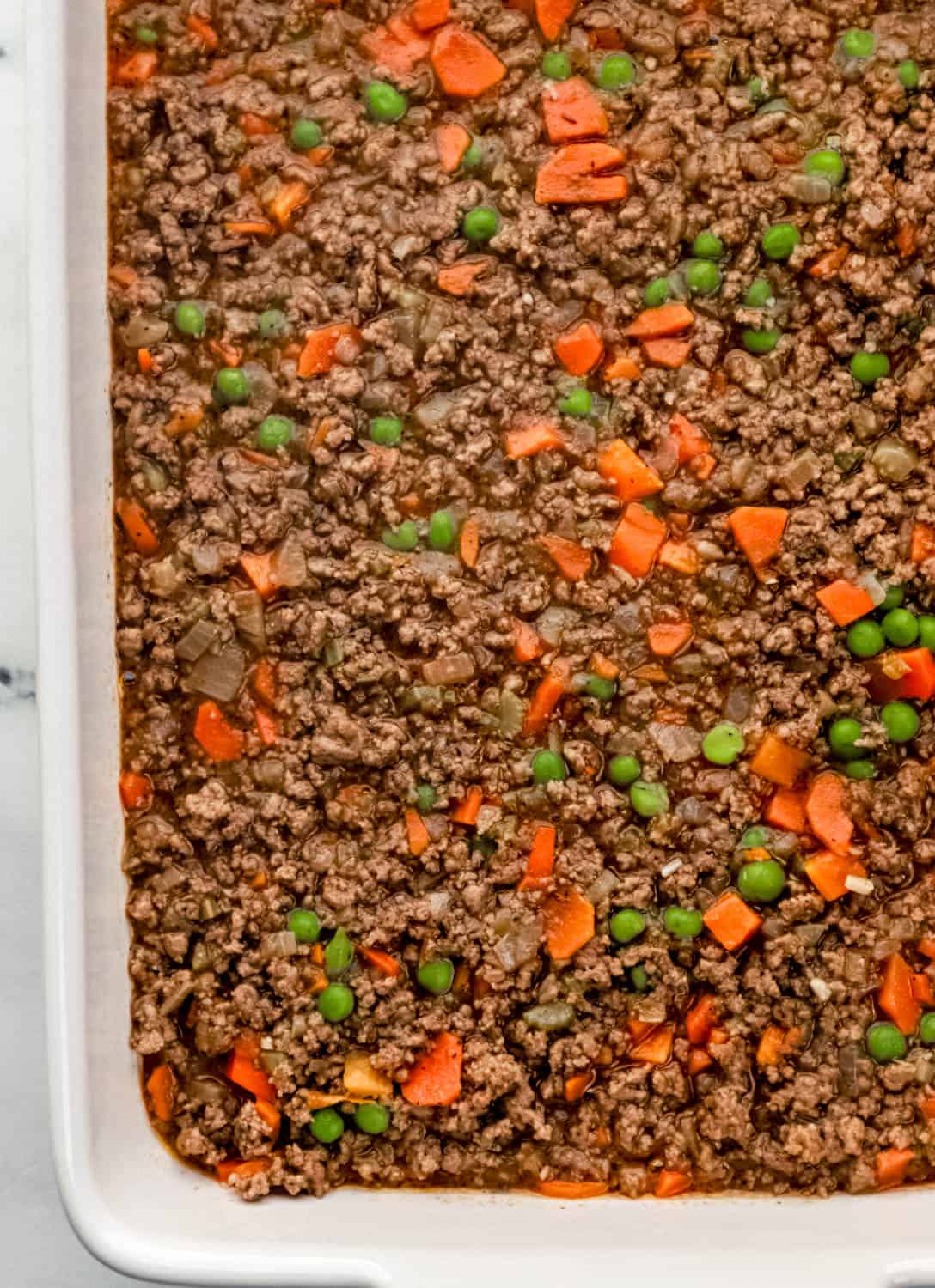 Ground beef filling added to the bottom of a white rectangle baking dish. 