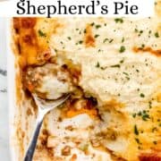 Overhead view of finished shepherd's pie in white baking dish with serving spoon in it on pin with text overlay.