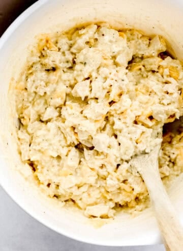 Casserole ingredients combined in a large white mixing bowl with wooden spoon.